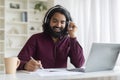 Distance Learning. Smiling Indian Man In Headphones Using Laptop And Taking Notes Royalty Free Stock Photo