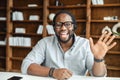 Black friendly man wearing headset waving hand to camera sitting indoors Royalty Free Stock Photo