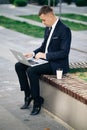 Distance working. Isolated man in a suit. Handsome young businessman sitting outdoors working with his laptop. Crisis