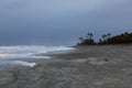 Distant couple walking on the coastline of a sandy beach in a storm, heavy surf and dark clouds