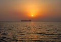 Distant crude oil taker on a sunset time against the sun in calm sea waters