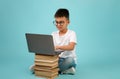 Distant Learning. Asian Schoolboy In Eyeglasses Using Laptop Placed On Book Stack