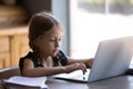 Concentrated little girl studying online doing homework on laptop