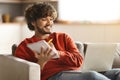 Distant Learning. Smiling indian guy using laptop and taking notes to notepad Royalty Free Stock Photo