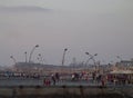 Distant look of Tel Aviv's port boardwalk at sunset with many people sitting, walking, doing leisure activities, and lamps