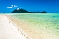 A distant man strolling along the white sandy beach on a deep blue sky along remote island