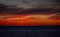 A distant off shore windfarm silhouetted against a vivid sunrise.