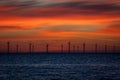 A distant off shore windfarm silhouetted against a vivid sunrise.
