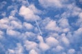 Distant passenger jet plane flying on high altitude through white clouds on blue sky leaving white smoke trace of Royalty Free Stock Photo