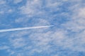 Distant passenger jet plane flying on high altitude through white clouds on blue sky leaving white smoke trace of Royalty Free Stock Photo