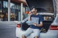 Distant plan of young man looking at map sitting in the truck of car. Royalty Free Stock Photo