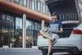 Distant plan of young man looking at map sitting in the truck of car. Royalty Free Stock Photo