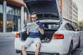 Distant plan of young man looking at map sitting in the truck of car. Royalty Free Stock Photo