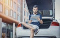 Distant plan of young man looking at map sitting in the truck of car. Royalty Free Stock Photo