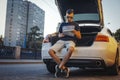 Distant plan of young man looking at map sitting in the truck of car. Royalty Free Stock Photo