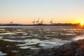 Distant port cranes and containers stacked at Sulphur Point as sun bursts across harbour at low tide