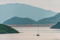 Distant sailboat floating on lake water on green mountains background. Scenic view of Plover Cove from Sha Lan villas at Shuen Wan