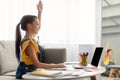 Girl sitting at table, using laptop, raising hand for answer Royalty Free Stock Photo