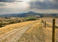 Distant storm clouds move above a mountain as seen from a dirt road along a fence in a Montana farm field