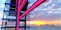 Distant sunrise behind concrete structure in the sea reflected in huge panoramic window of the exclusive designed apartment house