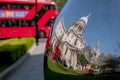 Distorted reflection of St Paul`s Cathedral, reflected in surface of mirror sculpture. Blurred red London bus in background.