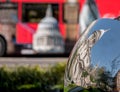 Distorted reflection of St Paul`s Cathedral, reflected in surface of mirror sculpture. Blurred red London bus in background.
