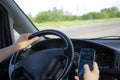 Distraction behind the wheel concept. A man dials a phone number on touch screen of smartphone while driving a car