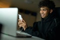 Distraction. Portrait of happy male student smiling and using smartphone while studying, working on laptop late at night Royalty Free Stock Photo