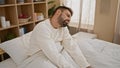 Distraught young hispanic man suffering from severe back injury, touching spinal column in agony while awake on his bedroom bed, Royalty Free Stock Photo