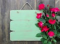 Distressed blank green sign with flower border of red roses hanging on rustic wood door Royalty Free Stock Photo