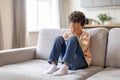 Distressed little black boy sitting on sofa, covering his face with hands