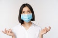 Distressed and miserable young asian woman in face mask, looking up, looking up sad, standing over white background