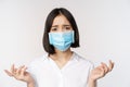 Distressed and miserable young asian woman in face mask, looking up, looking up sad, standing over white background