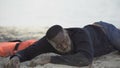 Distressed refugee lying on beach, looking with plea asking help, crash survivor