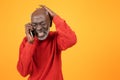 Distressed senior Black man in a red sweater, talking on a smartphone with a painful expression Royalty Free Stock Photo