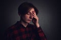 Distressed teenager boy mess in his head, pointing hand to forehead, eyes closed feeling pain, isolated on grey wall dark room