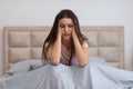Distressed woman sitting in bed, holding her head, showing signs of headache or intense stress Royalty Free Stock Photo