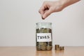 Distribution of cash savings concept. Hand puts coins to the glass money boxes with inscription `taxes`. Royalty Free Stock Photo