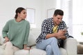 Distrustful woman peering into boyfriend`s smartphone. Jealousy in relationship