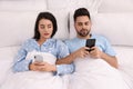 Distrustful young couple peering into each other`s smartphones in bed at home Royalty Free Stock Photo