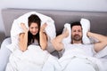 Couple covering their ears with pillow on bed