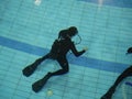 A diver in a neoprene wetsuit trains in the pool. A conrol of inexperienced divers