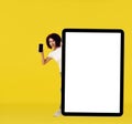 Diverse African American young woman looking out behind big, huge digital tablet pc with white screen and showing phone Royalty Free Stock Photo