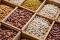 A diverse assortment of beans and legumes in wooden containers, including yellow, pink, and white varieties, presented