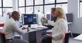 Diverse business people sitting using computer and takling at desk in office