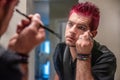 Diverse caucasian man with spiked pink hair applying eyeliner in the mirror Royalty Free Stock Photo