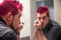 Diverse caucasian man with spiked pink hair applying eyeliner in the mirror Royalty Free Stock Photo