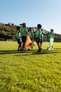 Diverse children collecting plastic high fiving in sunny elementary school sports field, copy space Royalty Free Stock Photo