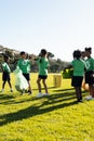 Diverse children collecting plastic high fiving in sunny elementary school sports field, copy space Royalty Free Stock Photo