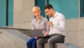 Diverse colleagues Caucasian woman and arabic Hispanic man sitting outdoors looking in laptop successful win